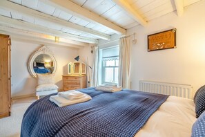 Ein Schlafzimmer mit Bett, Kommode, Spiegel und Fenster.
