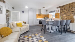 Un espacio habitable pequeño con kitchenette, un sofá con una manta amarilla y un tapete estampado.