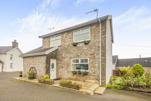 A stone house with a front door, two windows, and a small porch with planters.