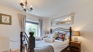 Ein Schlafzimmer mit Bett, Nachttisch, Lampe und einem Fenster mit Vorhängen.