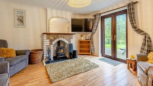 Ein gemütliches Wohnzimmer mit Kamin aus Stein, Holzboden und einem großen Fenster mit Vorhängen.
