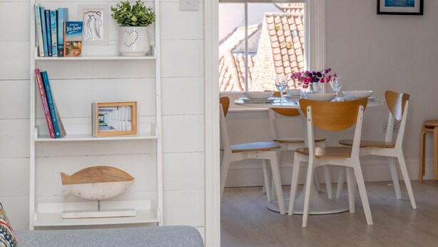 Ein gemütliches Zimmer mit Bücherregal, einem Essbereich mit Tisch und Stühlen sowie Blick ins Freie.