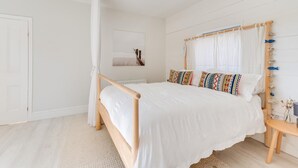 Ein Schlafzimmer mit einem hölzernen Bett, weißer Bettwäsche, einem Nachttisch mit einer Vase und einem Fenster mit Vorhängen.