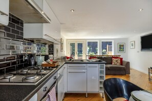 Eine moderne Küche mit einer zentralen Kochinsel, einem Essbereich mit einer Couch und einem großen Fenster mit Blick ins Freie.