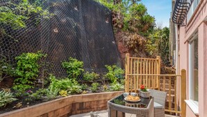 Een terras met tafel en stoelen, omgeven door een tuin met diverse planten en een houten hek.