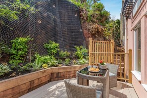 Eine Terrasse mit Tisch und Stühlen, umgeben von einem Garten mit verschiedenen Pflanzen und einem Holzzaun.