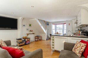 Ein modernes Wohnzimmer mit Flachbildfernseher, grauen Sofas und Holzboden.