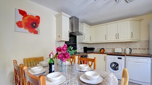 Una cocina moderna con armarios blancos, microondas, lavadora y comedor con una mesa dispuesta para dos.