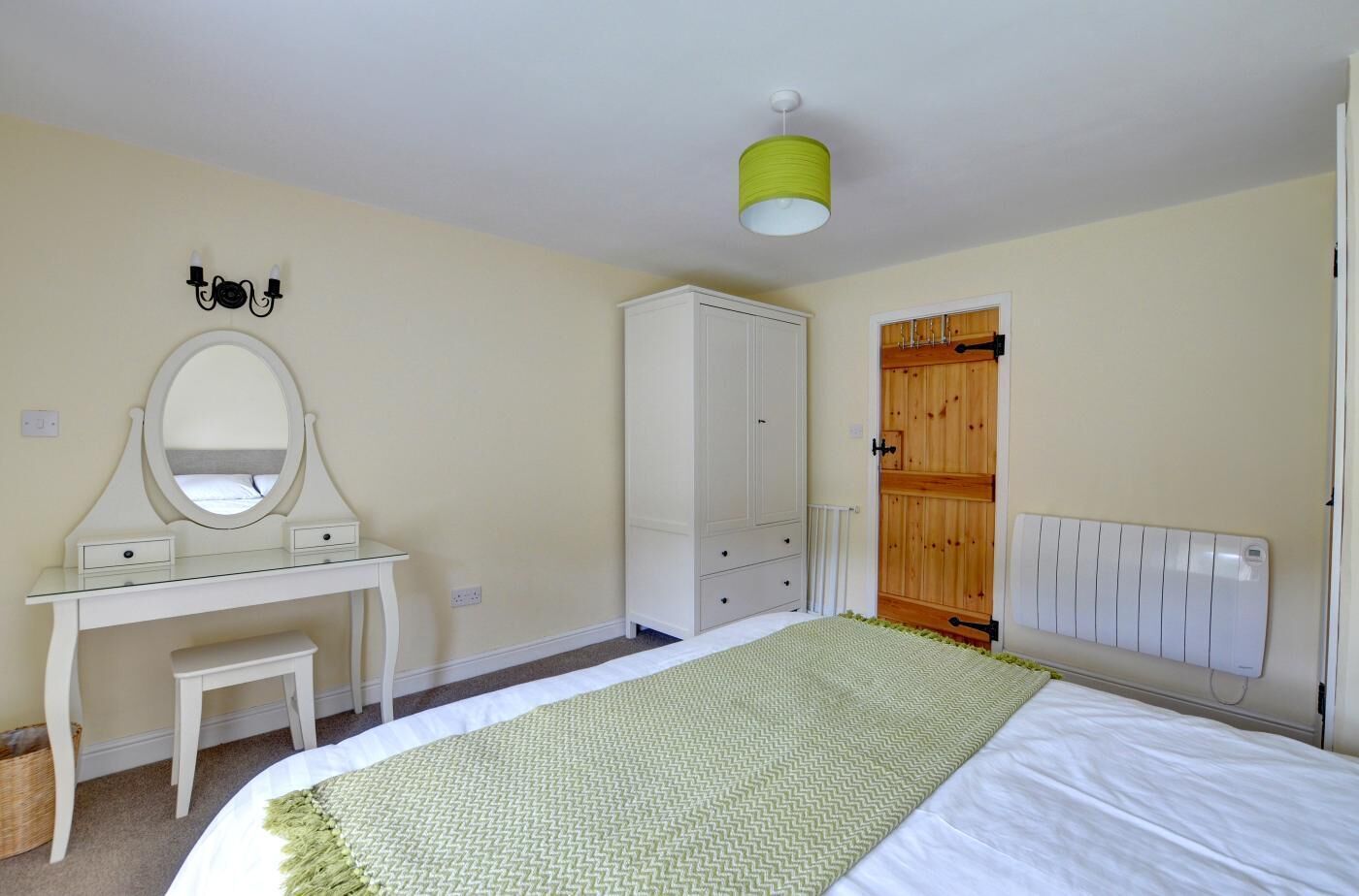 A bedroom with a bed, a white dresser with a mirror, a wooden wardrobe, and a radiator.
