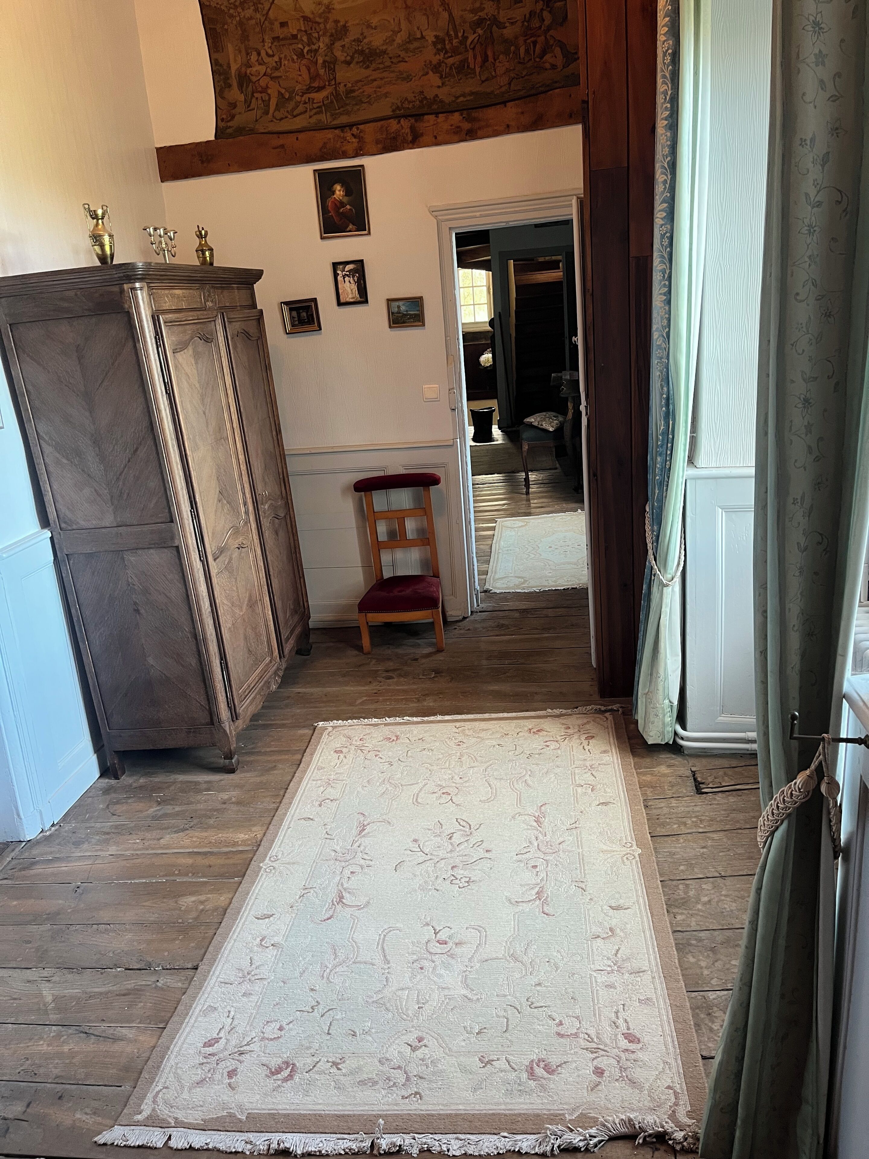 Ein Zimmer mit Holzboden, einem großen Teppich, einem Holzschrank und einem Stuhl.