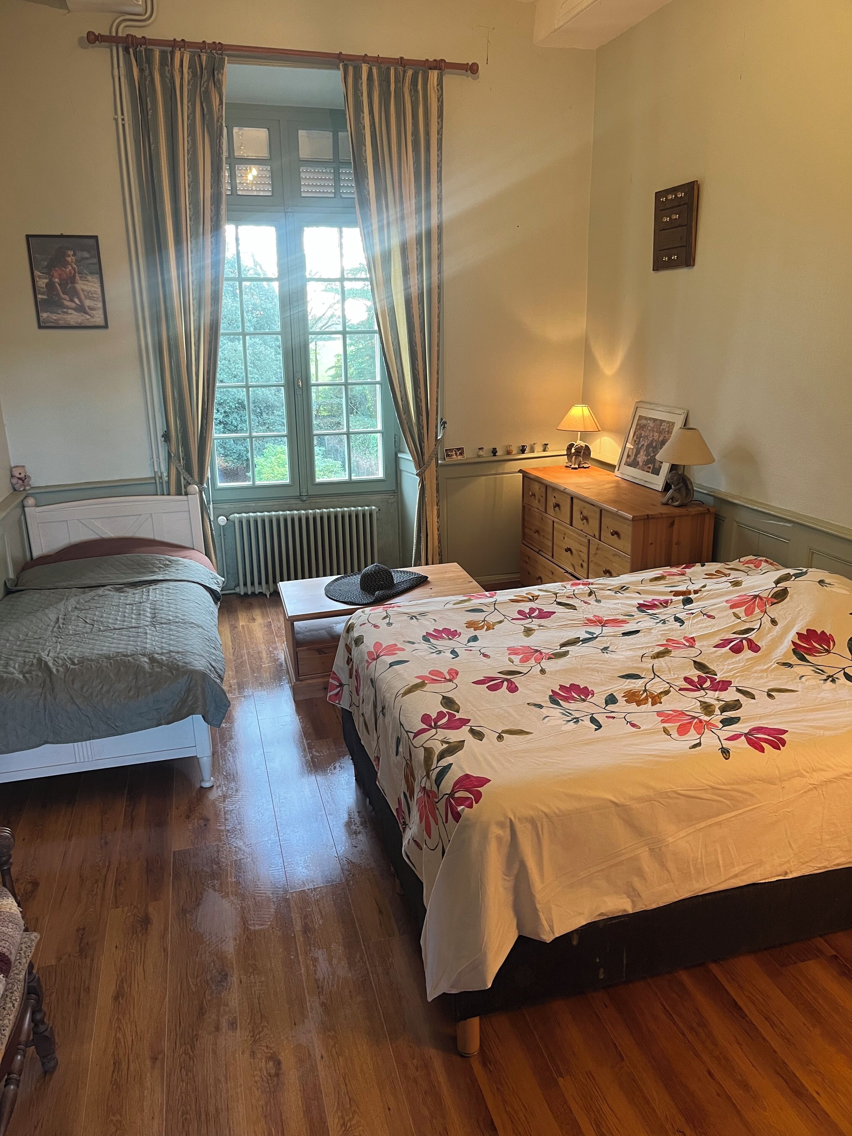 Une chambre avec deux lits, une commode en bois, un radiateur et une fenêtre avec des rideaux.