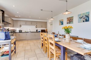 Une cuisine moderne avec des meubles blancs, une table à manger dressée pour six personnes et un vase de fleurs jaunes posé sur la table.