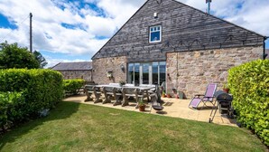 Un bâtiment en pierre doté d’un grand patio, d’un espace extérieur aménagé avec des sièges et d’un coin barbecue.