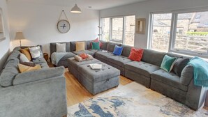 Un salon spacieux avec un grand canapé d’angle gris, une table basse et une grande fenêtre donnant sur l’extérieur.