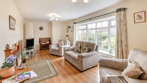 A living room with a sofa, armchair, TV, and a large window with curtains. - 2 Bed in Whitby (oc-w104) (Whitby)