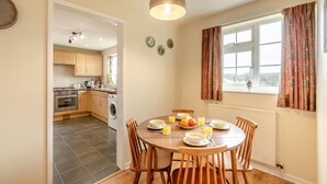 A kitchen with a dining table set for breakfast, a washing machine, and a window with curtains. - 2 Bed in Whitby (oc-w104) (Whitby)