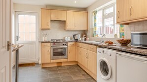A modern kitchen with wooden cabinets, a built-in oven, a microwave, and a washing machine. - 2 Bed in Whitby (oc-w104) (Whitby)