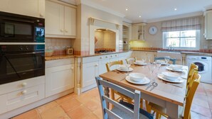 A modern kitchen with white cabinetry, a dining table set for six, and a built-in oven. - 3 Bed in Southwold (oc-5sr) (Southwold)