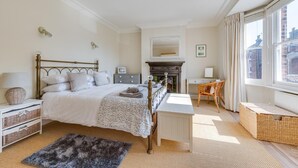 A bedroom with a bed, bedside table, dresser, desk, chair, fireplace, and large window. - 3 Bed in Southwold (oc-5sr) (Southwold)