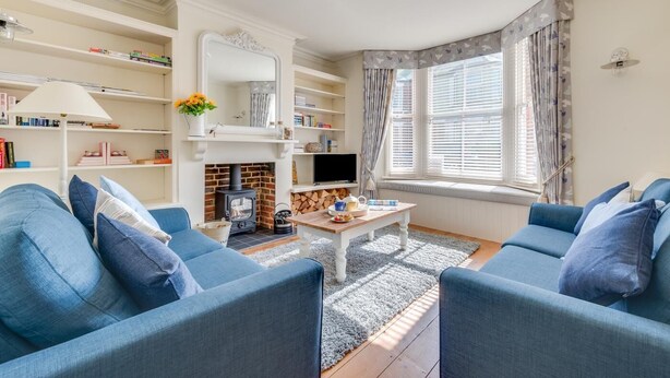 A cozy living room with a fireplace, blue sofas, a coffee table, and bookshelves. - 3 Bed in Southwold (oc-5sr) (Southwold)