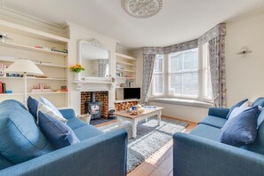 Un salon chaleureux avec une cheminée, des canapés bleus, une table basse et des étagères à livres.