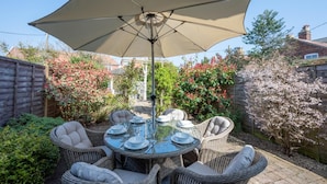 A round glass table with wicker chairs and a large beige umbrella in a garden setting. - 3 Bed in Southwold (oc-5sr) (Southwold)