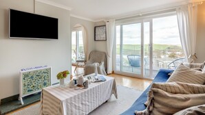 Amplia sala de estar con televisor grande, comedor con mesa puesta y balcón con mobiliario exterior.