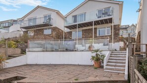 Una casa moderna de dos pisos con un balcón, un jardín pequeño y un patio empedrado.