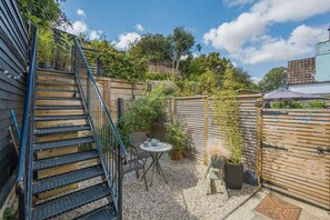 A backyard with a wooden fence, a metal staircase, a table with chairs, and potted plants. - 1 Bed in Woodbridge (oc-11ang) (Woodbridge)