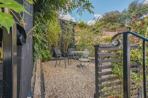 A garden area with a gravel path, a wooden gate, and outdoor seating with chairs and a table. - 1 Bed in Woodbridge (oc-11ang) (Woodbridge)