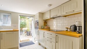 Een keuken met witte kasten, een houten aanrechtblad en uitzicht op de tuin door een open deur.