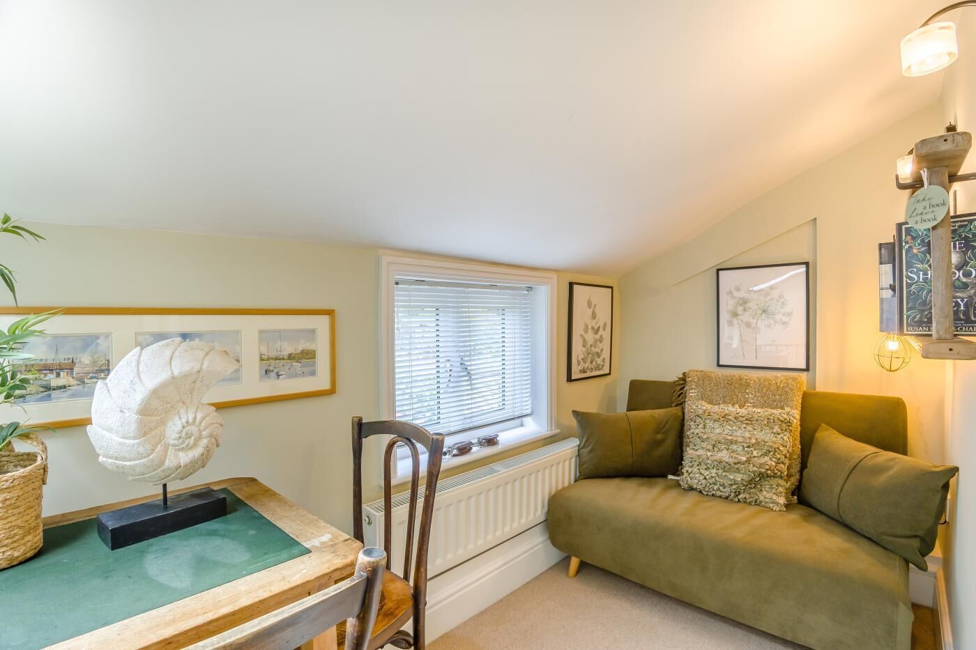 A cozy room with a green sofa, a wooden chair, a table with a sculpture, and framed pictures on the walls.