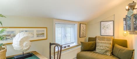 A cozy room with a green sofa, a wooden chair, a table with a sculpture, and framed pictures on the walls.