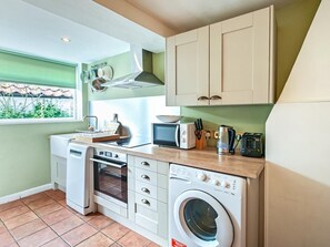 A compact kitchen with a built-in oven, microwave, and washing machine, a window with a view, and a green wall. - 2 Bed in Burnham Market (oc-j33432) (Burnham Market)
