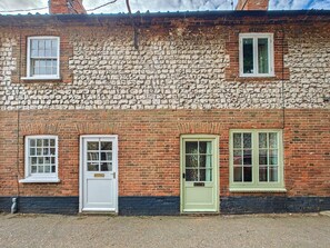Un bâtiment en briques avec trois fenêtres et une porte, doté d’une façade en pierre et d’une base noire.