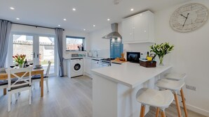 A modern kitchen with a central island, built-in appliances, and a large wall clock. - 2 Bed in Swanage (oc-wy606) (Swanage)
