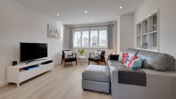 A modern living room with a flat-screen TV, a grey sofa, a small table with a vase, and a chair with a cushion. - 2 Bed in Swanage (oc-wy606) (Swanage)
