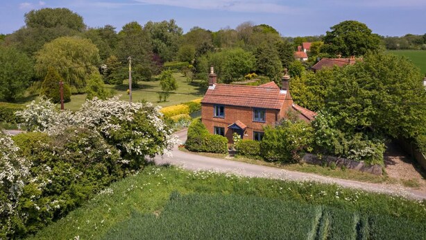 Una casa di campagna con facciata in mattoni, immersa nel verde e con cielo sereno.