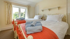 Una camera d'albergo con due letti, una finestra con tende, un comodino con una lampada e uno scaffale sopra i letti.