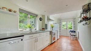 Una cucina moderna con mobili bianchi, una lavastoviglie Bosch, un piano cottura e un lavello. Si vede una finestra con vista su piante.