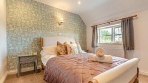 A bedroom with a large bed, a nightstand, a wall-mounted lamp, and a window with curtains. - 3 Bed in Petrockstow (oc-n33541) (Petrockstow)