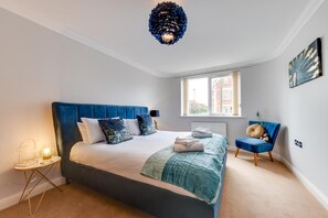A bedroom with a large bed, a chair, a window, and a unique ceiling light fixture.