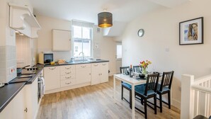 A modern kitchen with a dining area, wooden flooring, and a pendant light. - 2 Bed in Whitby (oc-w402) (Whitby)