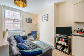 A compact living space with a sofa, a chair, a television, and a small kitchen area. - 2 Bed in Whitby (oc-w402) (Whitby)