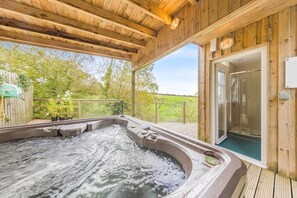 Une terrasse en bois avec un jacuzzi, une douche en verre et une vue sur un champ verdoyant.