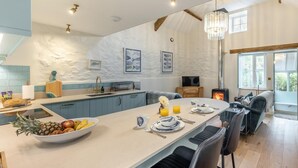A modern kitchen with a central island, a dining area with chairs, and a fireplace. - 1 Bed in Moylegrove (oc-b33506) (Cardigan)