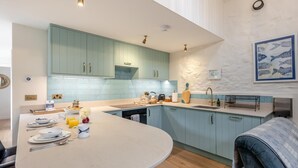 A modern kitchen with light blue cabinets, a central island, and a dining area with a round table. - 1 Bed in Moylegrove (oc-b33506) (Cardigan)