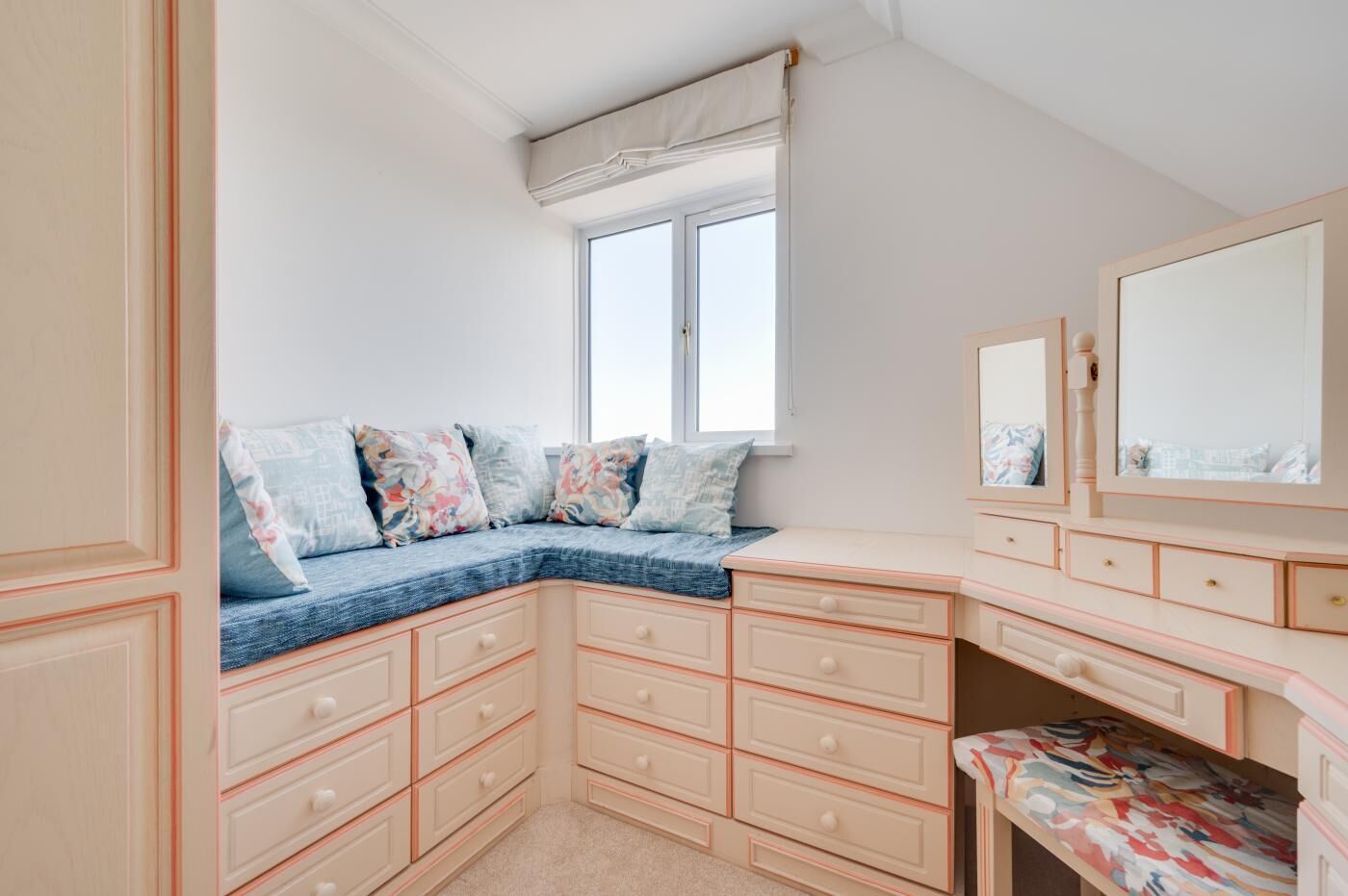 Une chambre dotée d’une banquette intégrée, de nombreux tiroirs, d’un miroir et d’une fenêtre.