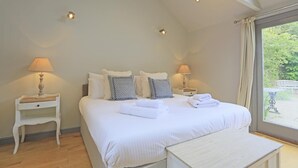 Ein Schlafzimmer mit einem großen Bett, zwei Nachttischen mit Lampen, einer Bank am Fußende des Bettes und einem Fenster mit Blick auf Grünflächen.