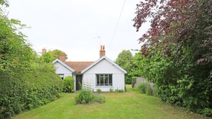 Ein eingeschossiges Haus mit weißer Fassade und rotem Ziegeldach, umgeben von einem gepflegten Garten und dichter Bepflanzung.
